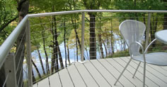 Residential stainless steel cable rail photo with light clay aluminum plank decking with a view of a lake by Versadeck Decking